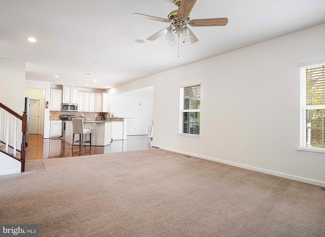 unfurnished living room with recessed lighting, baseboards, carpet, and stairs