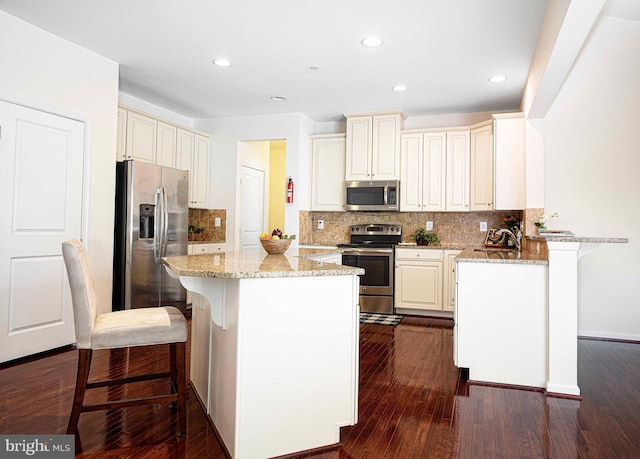 kitchen featuring a breakfast bar area, light stone counters, dark wood-style flooring, and stainless steel appliances