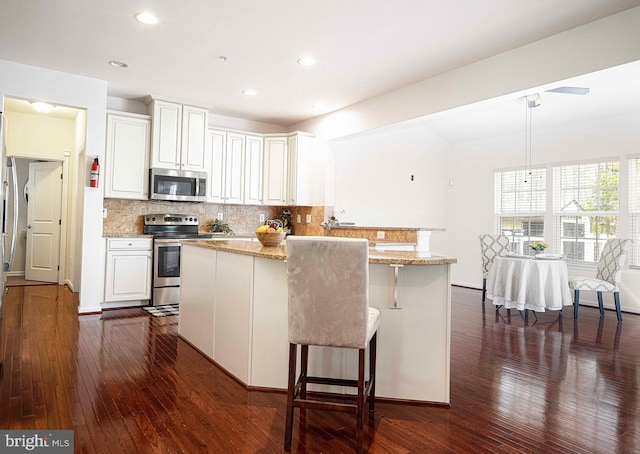 kitchen with dark wood finished floors, light stone counters, backsplash, and stainless steel appliances