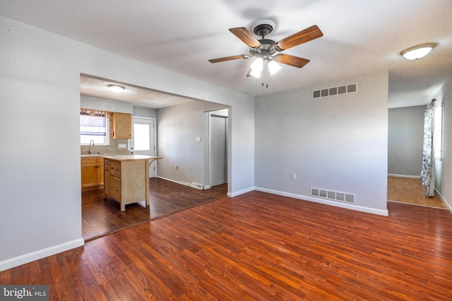 unfurnished living room with dark wood-style flooring, visible vents, a sink, and baseboards