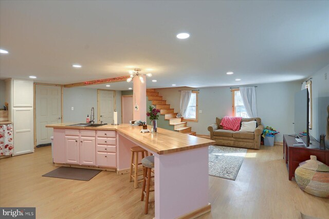 kitchen with a sink, wood counters, light wood-style floors, open floor plan, and a kitchen bar