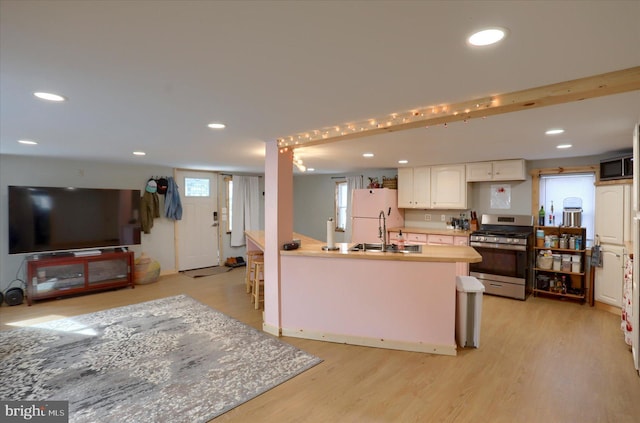 kitchen featuring stainless steel gas stove, light countertops, a sink, and freestanding refrigerator