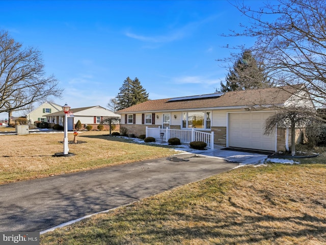 ranch-style home featuring solar panels, aphalt driveway, an attached garage, covered porch, and a front lawn