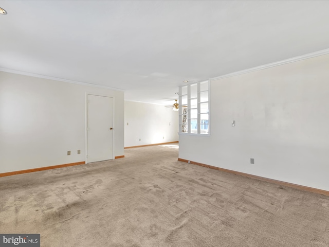 empty room with a ceiling fan, light colored carpet, crown molding, and baseboards