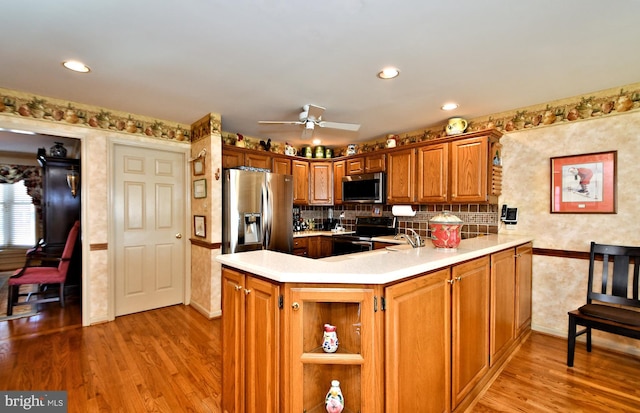 kitchen with stainless steel appliances, a peninsula, light wood-style floors, light countertops, and brown cabinets