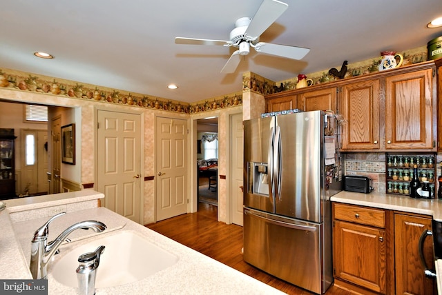 kitchen with dark wood-style flooring, stainless steel refrigerator with ice dispenser, light countertops, brown cabinetry, and a sink