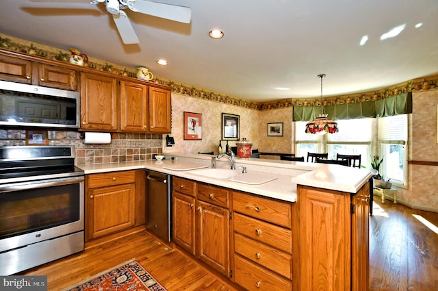 kitchen featuring stainless steel appliances, a peninsula, a sink, hanging light fixtures, and light countertops