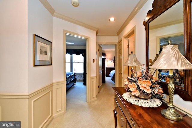 corridor featuring a decorative wall, recessed lighting, light colored carpet, ornamental molding, and wainscoting