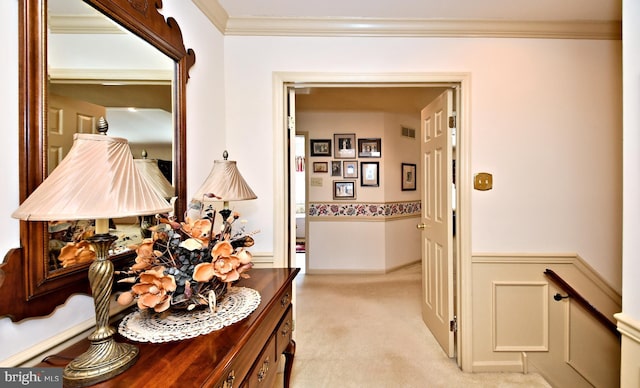 hall with wainscoting, light carpet, crown molding, and visible vents