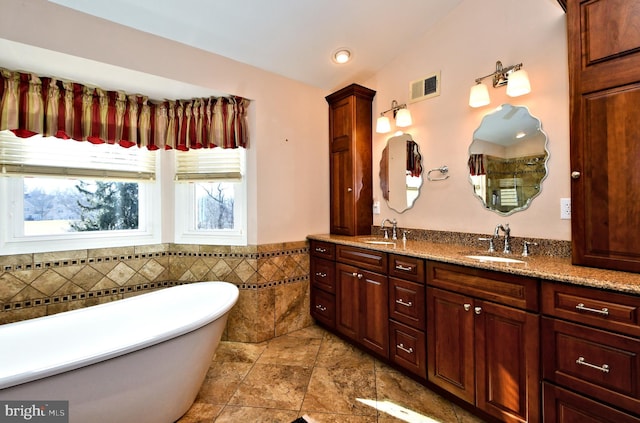 bathroom with double vanity, a freestanding bath, visible vents, and a sink