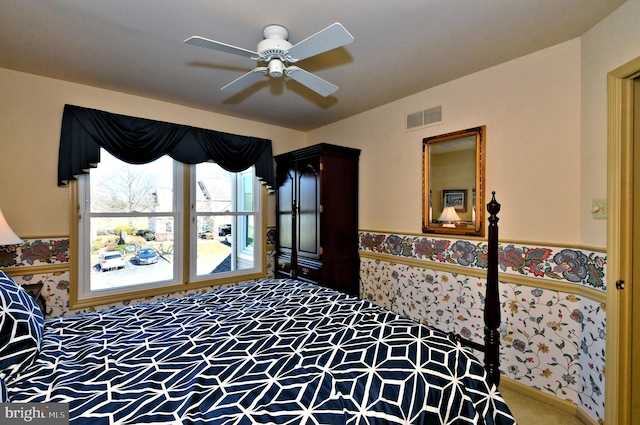 bedroom with carpet, a wainscoted wall, visible vents, and ceiling fan