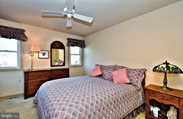 bedroom featuring light carpet, multiple windows, visible vents, and a ceiling fan