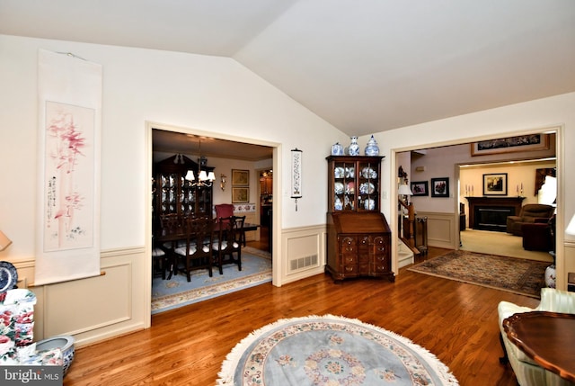 living area featuring visible vents, wainscoting, wood finished floors, vaulted ceiling, and a fireplace