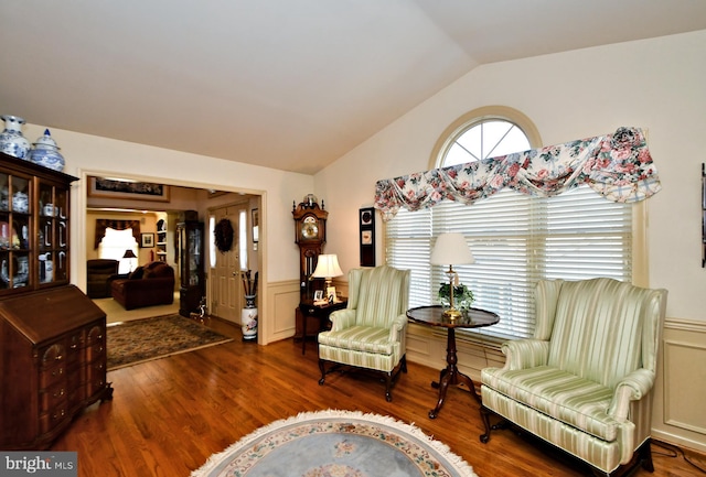 sitting room featuring lofted ceiling, dark wood-style flooring, wainscoting, and a decorative wall