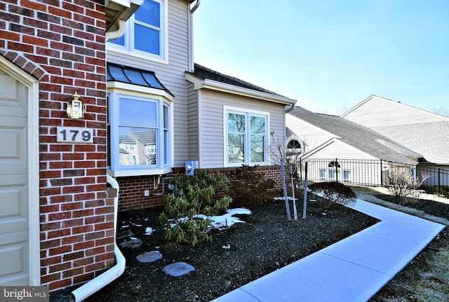 exterior space featuring an attached garage, brick siding, a shingled roof, fence, and a standing seam roof