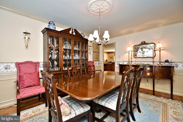 dining room with ornamental molding, a chandelier, a wainscoted wall, and light wood-style floors