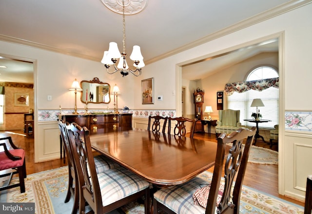 dining room featuring light wood-style floors, ornamental molding, wainscoting, vaulted ceiling, and a chandelier