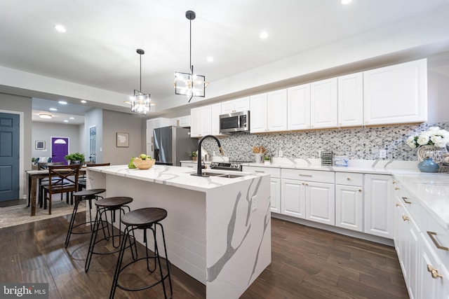 kitchen with white cabinets, an island with sink, appliances with stainless steel finishes, light stone counters, and pendant lighting