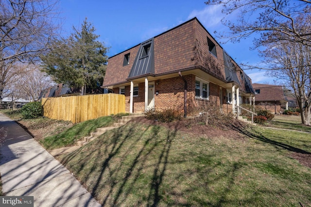 view of side of property featuring mansard roof, a lawn, roof with shingles, fence, and brick siding