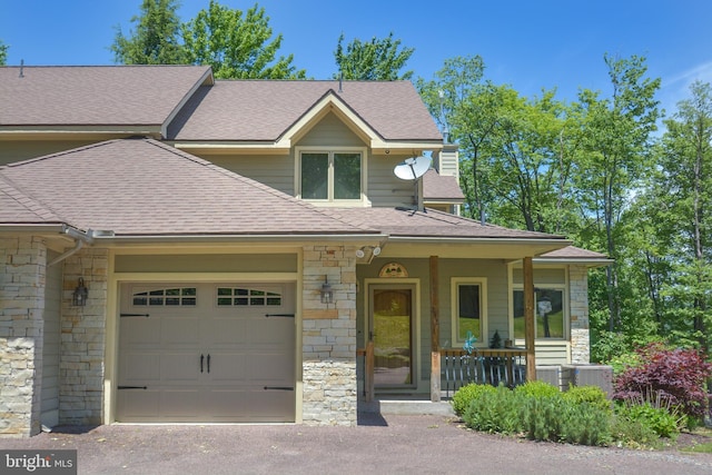 view of front of home with roof with shingles, central air condition unit, a porch, an attached garage, and stone siding