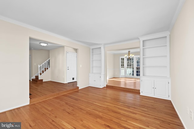 unfurnished living room with built in features, a notable chandelier, ornamental molding, light wood-type flooring, and stairs