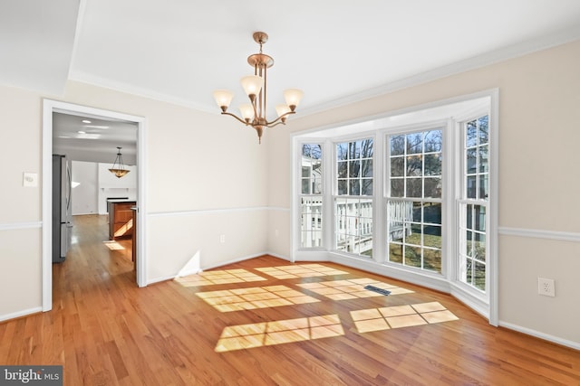 unfurnished dining area with baseboards, ornamental molding, a chandelier, and wood finished floors