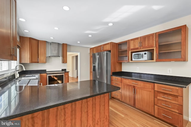 kitchen with wall chimney exhaust hood, appliances with stainless steel finishes, a peninsula, light wood-type flooring, and a sink