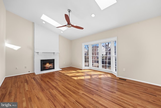 unfurnished living room featuring ceiling fan, vaulted ceiling with skylight, wood finished floors, and visible vents