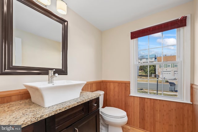 half bathroom featuring a wainscoted wall, vanity, toilet, and wooden walls