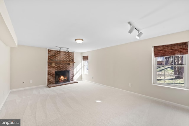 unfurnished living room featuring a brick fireplace, baseboards, carpet flooring, and track lighting