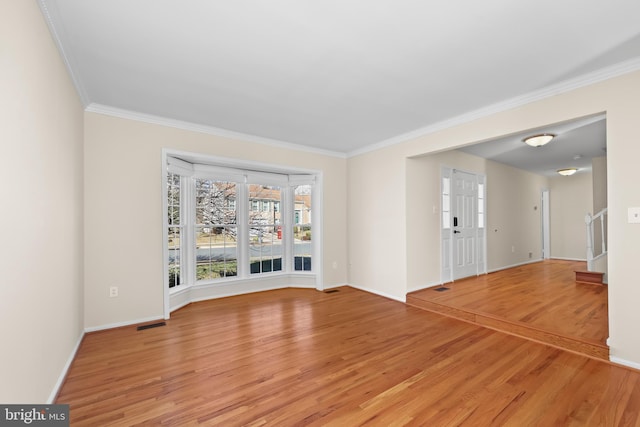 spare room with light wood finished floors, visible vents, baseboards, and crown molding