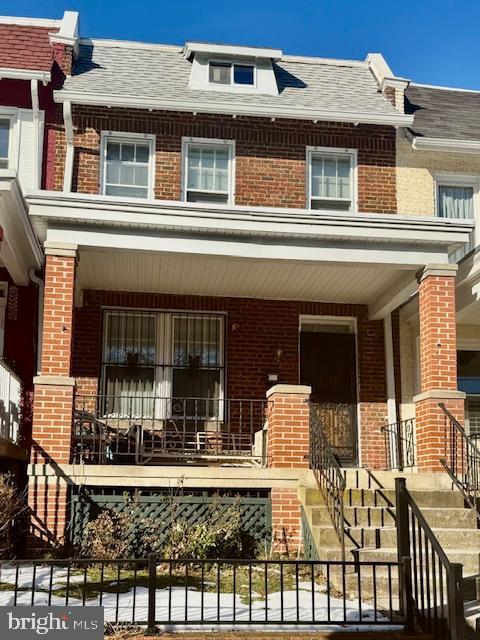 townhome / multi-family property with covered porch, roof with shingles, stairs, and brick siding