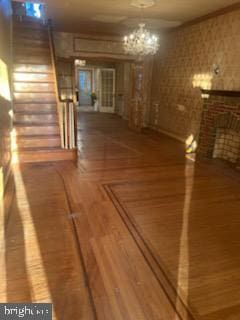 unfurnished living room featuring stairs, a chandelier, a fireplace, and wood finished floors