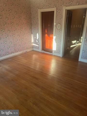 empty room featuring baseboards, wood finished floors, and wallpapered walls