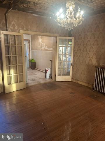 empty room with a chandelier, wood finished floors, and radiator