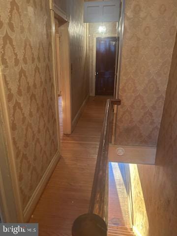 corridor featuring baseboards, light wood-style floors, and wallpapered walls