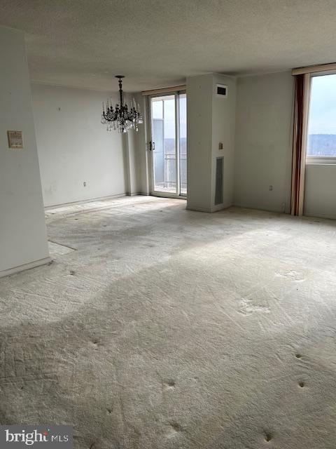 spare room with light carpet, an inviting chandelier, and a textured ceiling