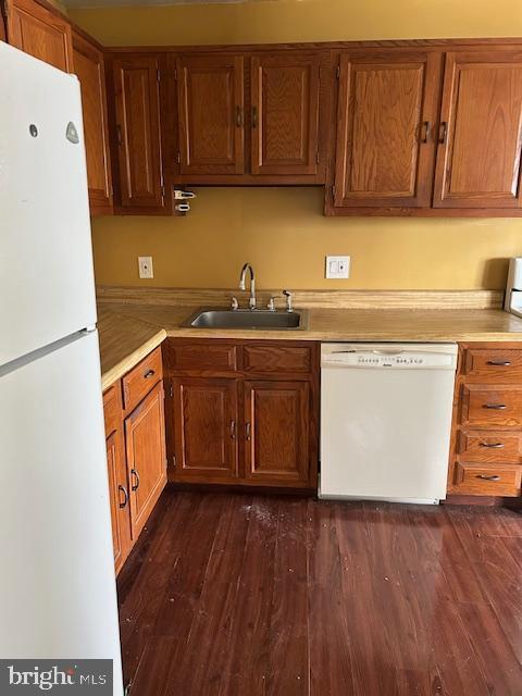 kitchen with brown cabinetry, white appliances, light countertops, and a sink