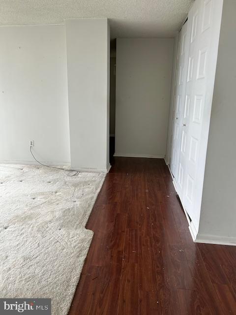 corridor featuring a textured ceiling, dark wood finished floors, and baseboards