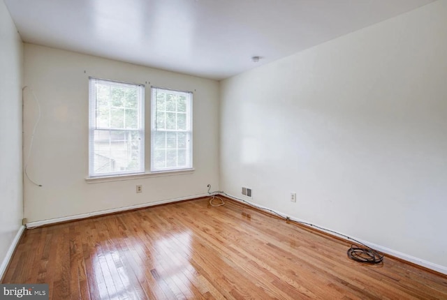 empty room featuring wood-type flooring, visible vents, and baseboards