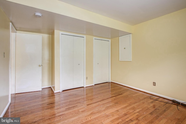 unfurnished bedroom with multiple closets, baseboards, and light wood finished floors