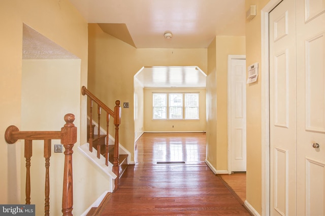 entrance foyer featuring baseboards, stairs, arched walkways, and wood finished floors