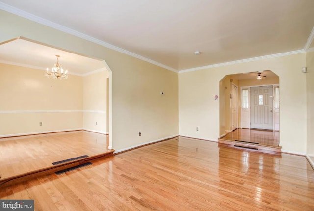 unfurnished living room featuring arched walkways, crown molding, wood finished floors, and a notable chandelier