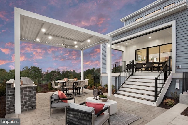 patio terrace at dusk featuring grilling area, stairway, outdoor dining area, and a ceiling fan