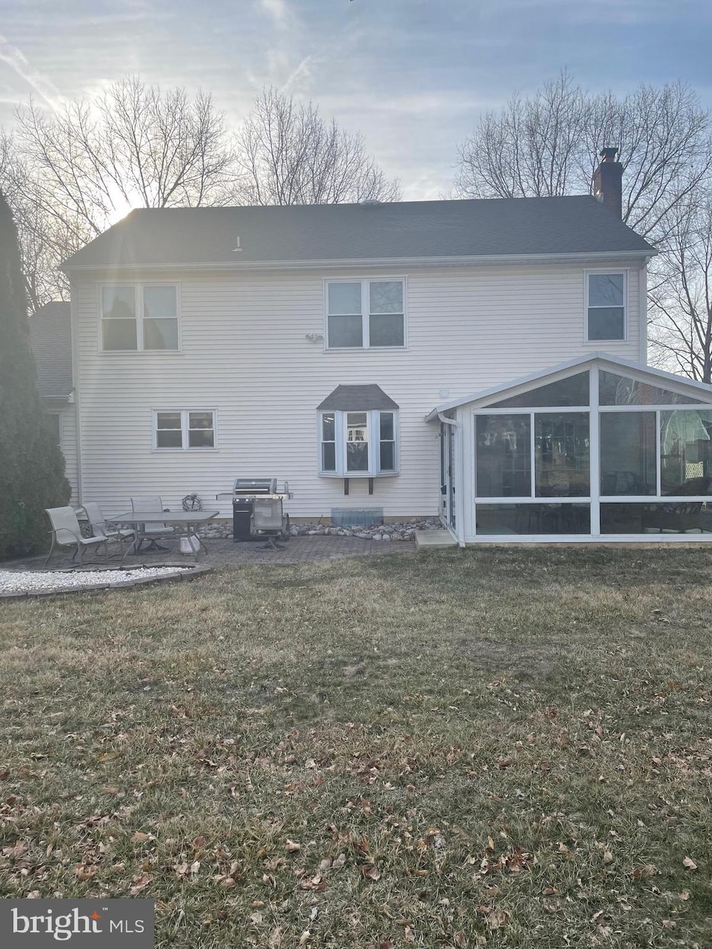 rear view of house with a sunroom, a patio area, a lawn, and a chimney