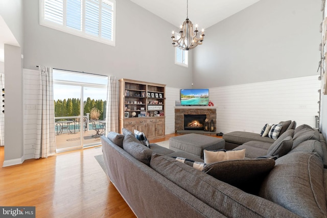 living area featuring high vaulted ceiling, light wood-style flooring, a chandelier, and a stone fireplace