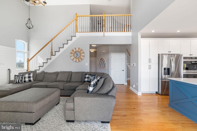 living area featuring recessed lighting, stairway, a towering ceiling, light wood-style floors, and baseboards