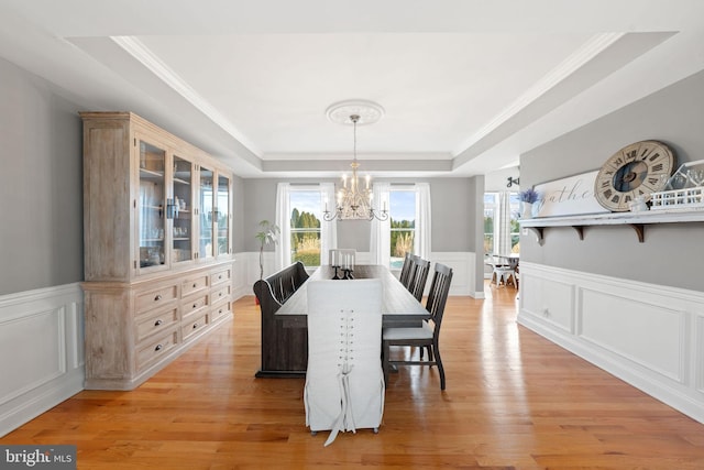 dining space with a raised ceiling, a wainscoted wall, a notable chandelier, and light wood finished floors