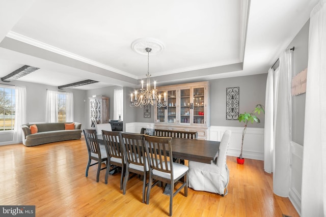 dining area featuring a wainscoted wall, a tray ceiling, a notable chandelier, and light wood-style floors