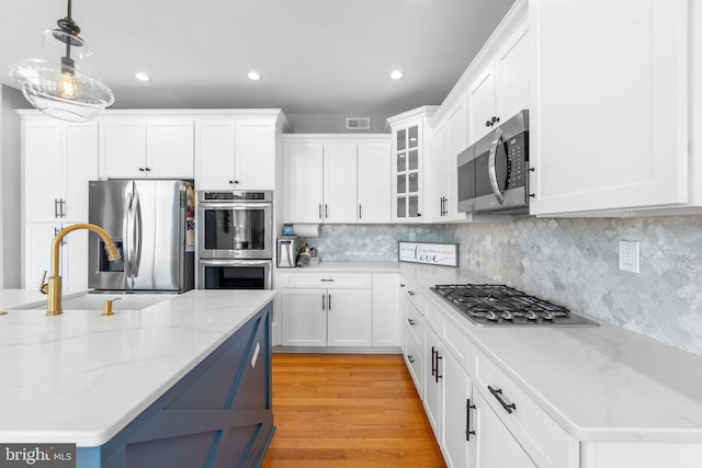 kitchen with appliances with stainless steel finishes, light wood-type flooring, white cabinets, and backsplash